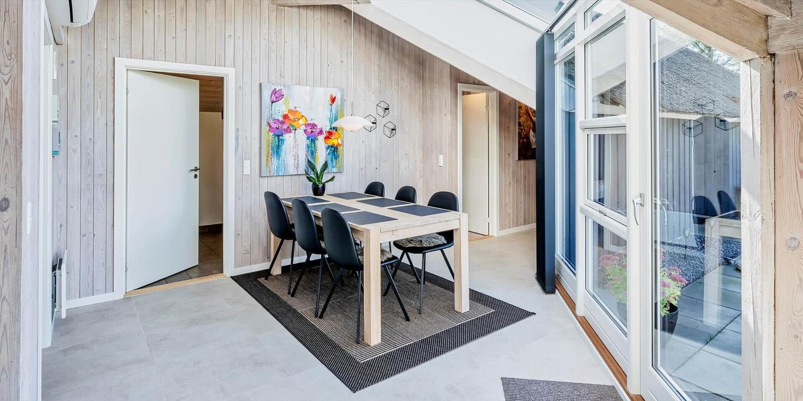 Essbereich mit Tisch, Stühlen und Wandbild. Glasfront führt auf die Terrasse.
