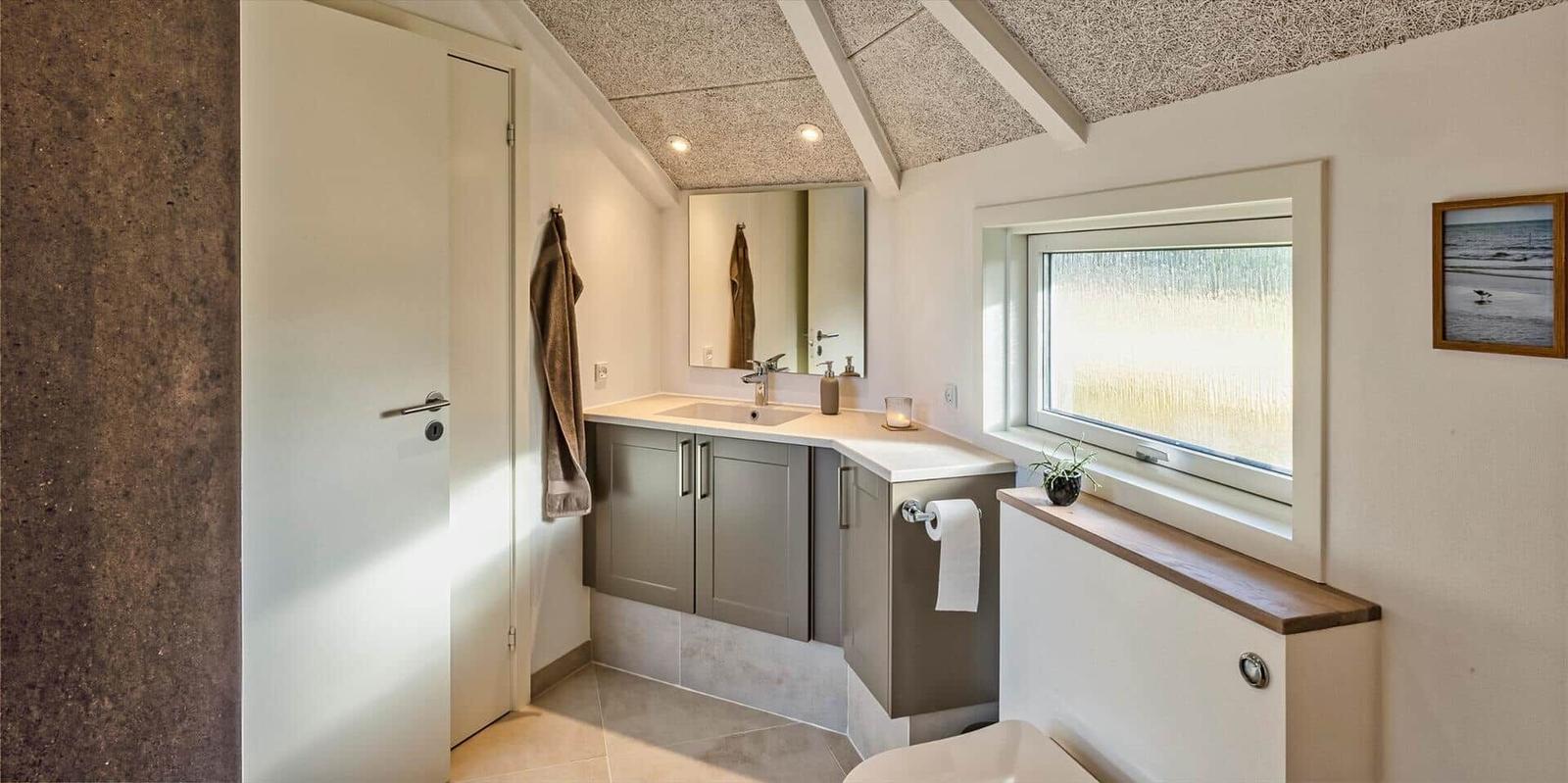 Badezimmer mit Waschbecken, Spiegel, Fenster und Toilette.