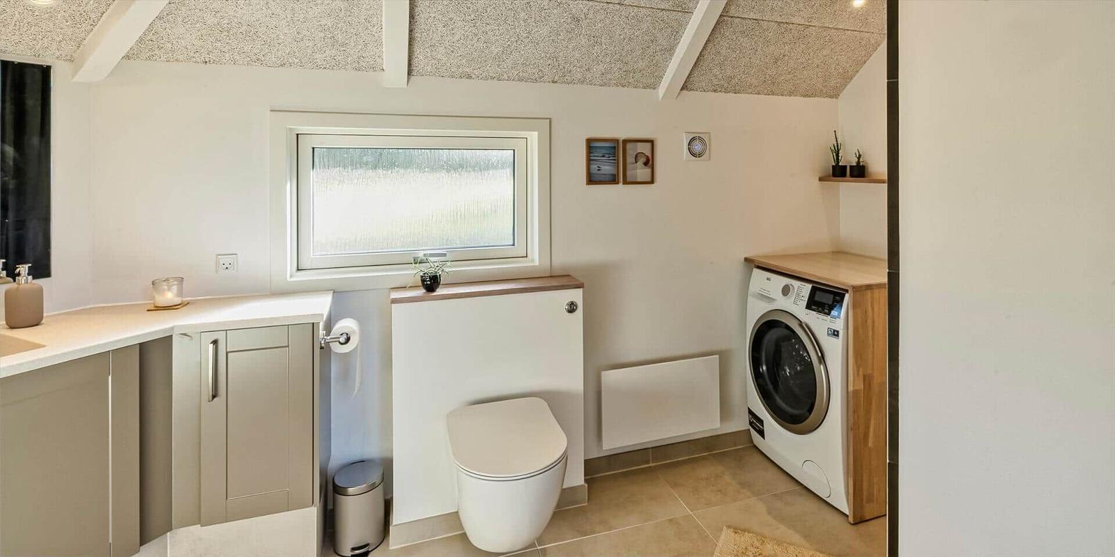Badezimmer mit Waschmaschine, Toilette und Waschbecken unter Dachschrägen.