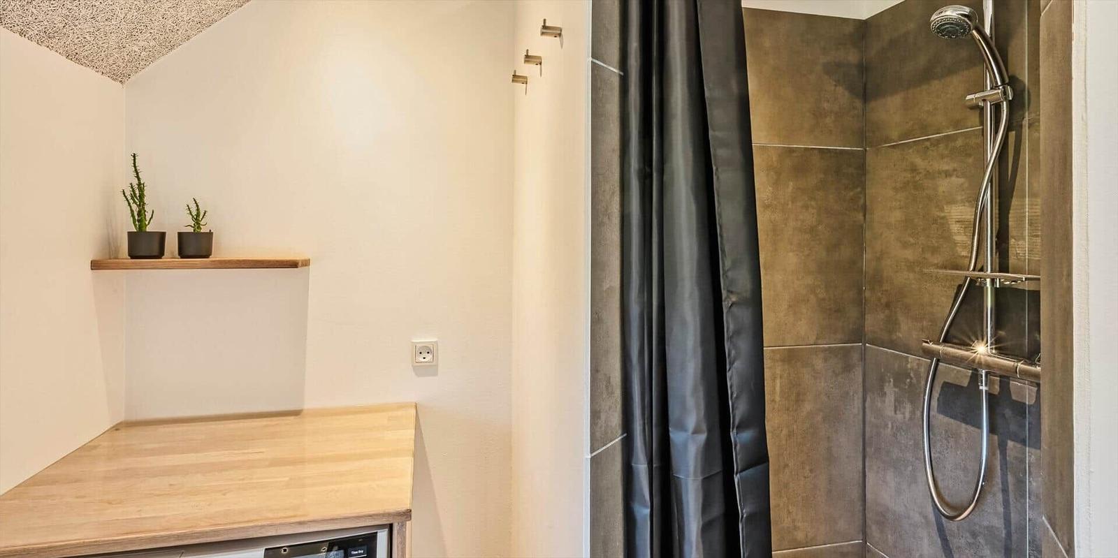 Dusche mit dunkler Plane und braunen Fliesen. Holzoberfläche und Pflanzen auf Regal.
