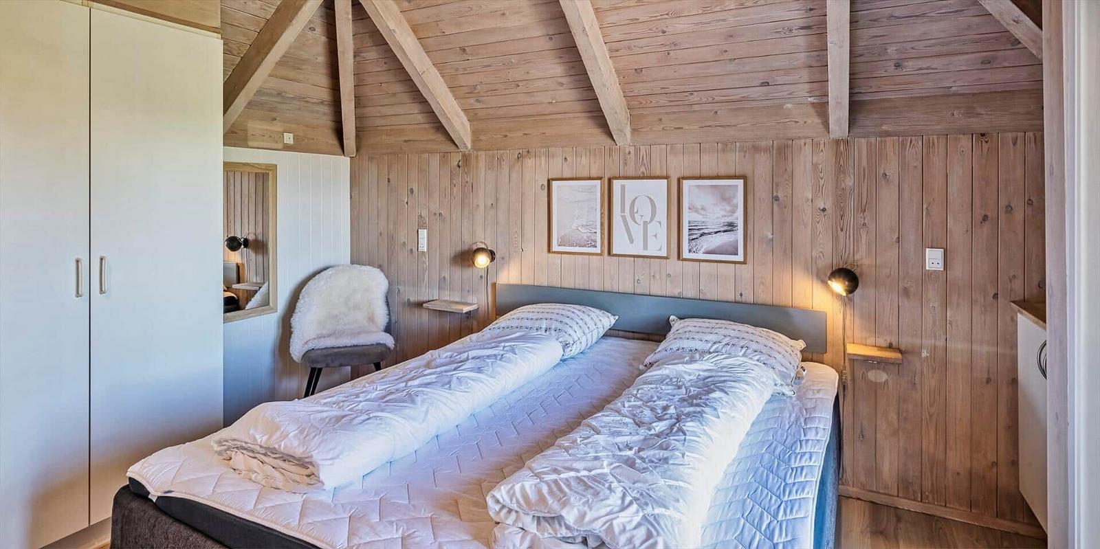 Schlafzimmer mit Doppelbett, Holzwand und Deckenbalken. An der Wand hängen drei Bilder.