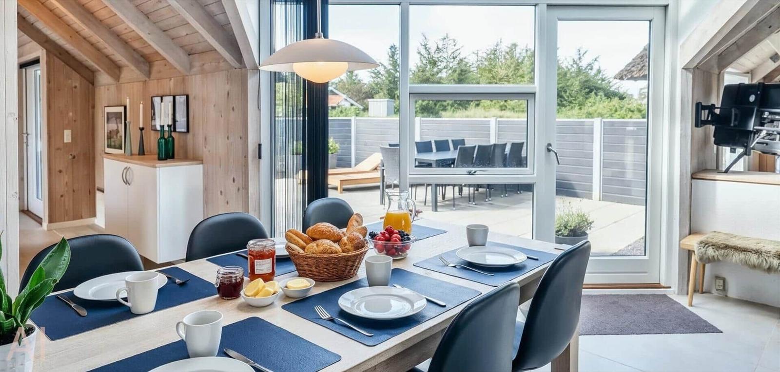 Esstisch mit Frühstück im Haus. Durchgang zum Balkon mit Gartenmöbeln.