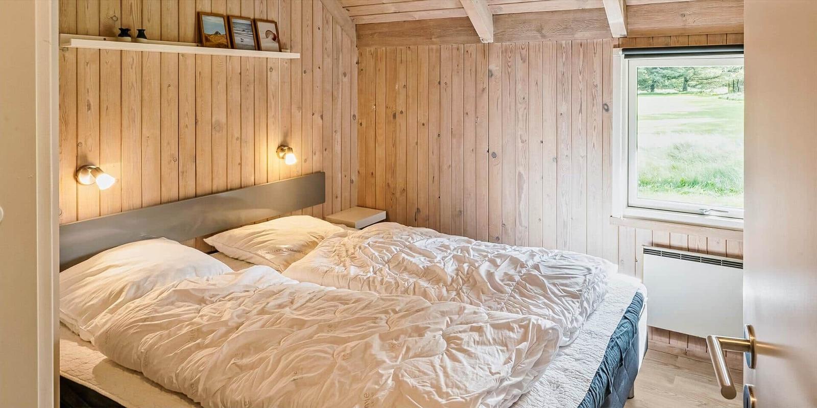 Schlafzimmer mit Holzwand, Bett und Fenster mit Blick auf Grasland.