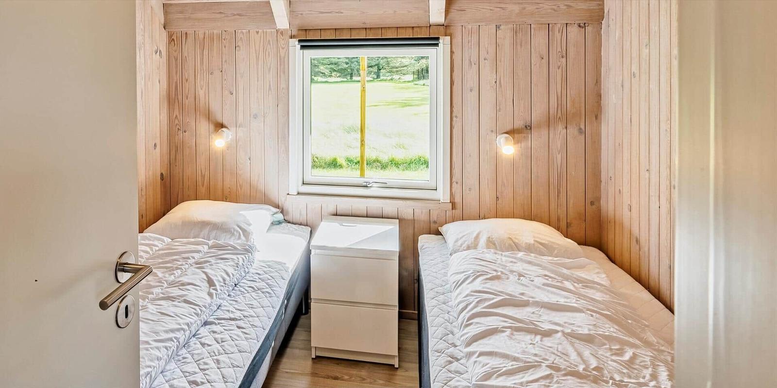 Zwei Betten mit weißen Bettwäsche, Holzwände und Fenster mit Blick auf Grünfläche.