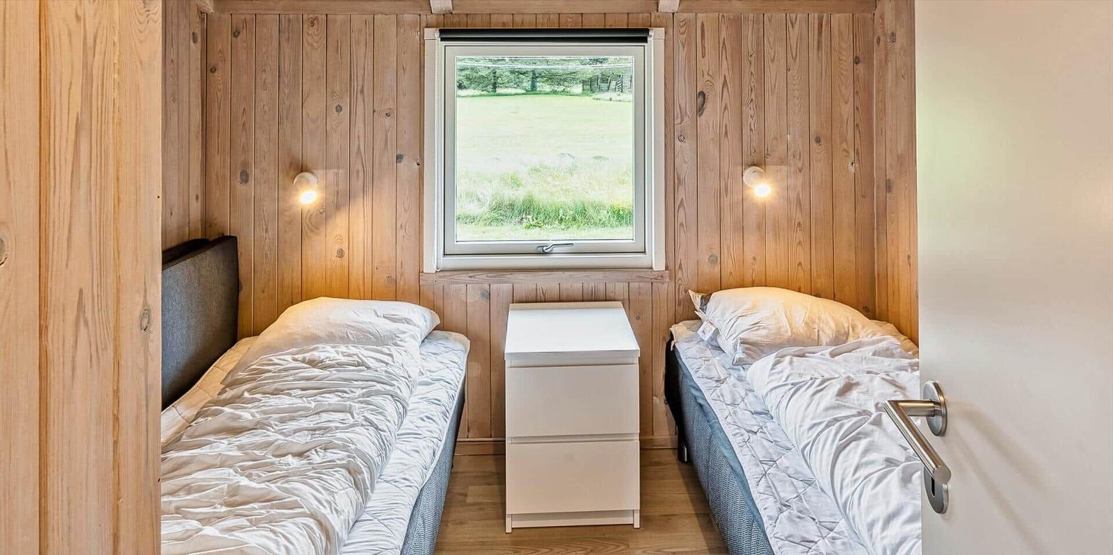 Zwei Einzelbetten mit Nachttisch und Fenster zur grünen Landschaft.