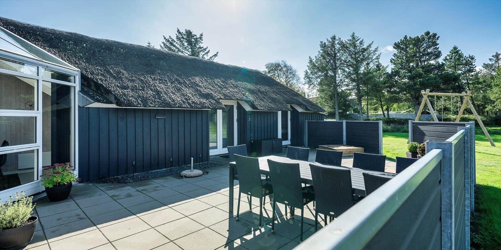 Terrasse mit Tisch und Stühlen vor einem Haus mit Strohdach und Garten.