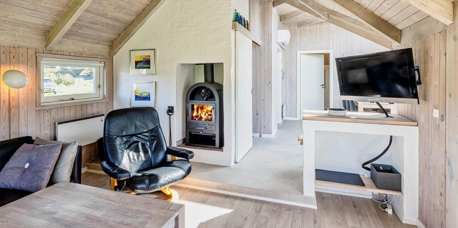 Wohnraum mit Kamin, schwarzer Ledersessel und Fernseher an der Wand.