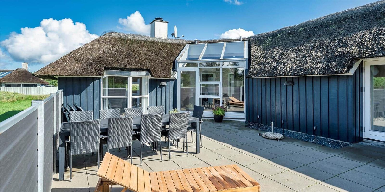 Terrasse mit Tisch, Stühlen und Sonnenliege vor einem Haus mit Strohdach.