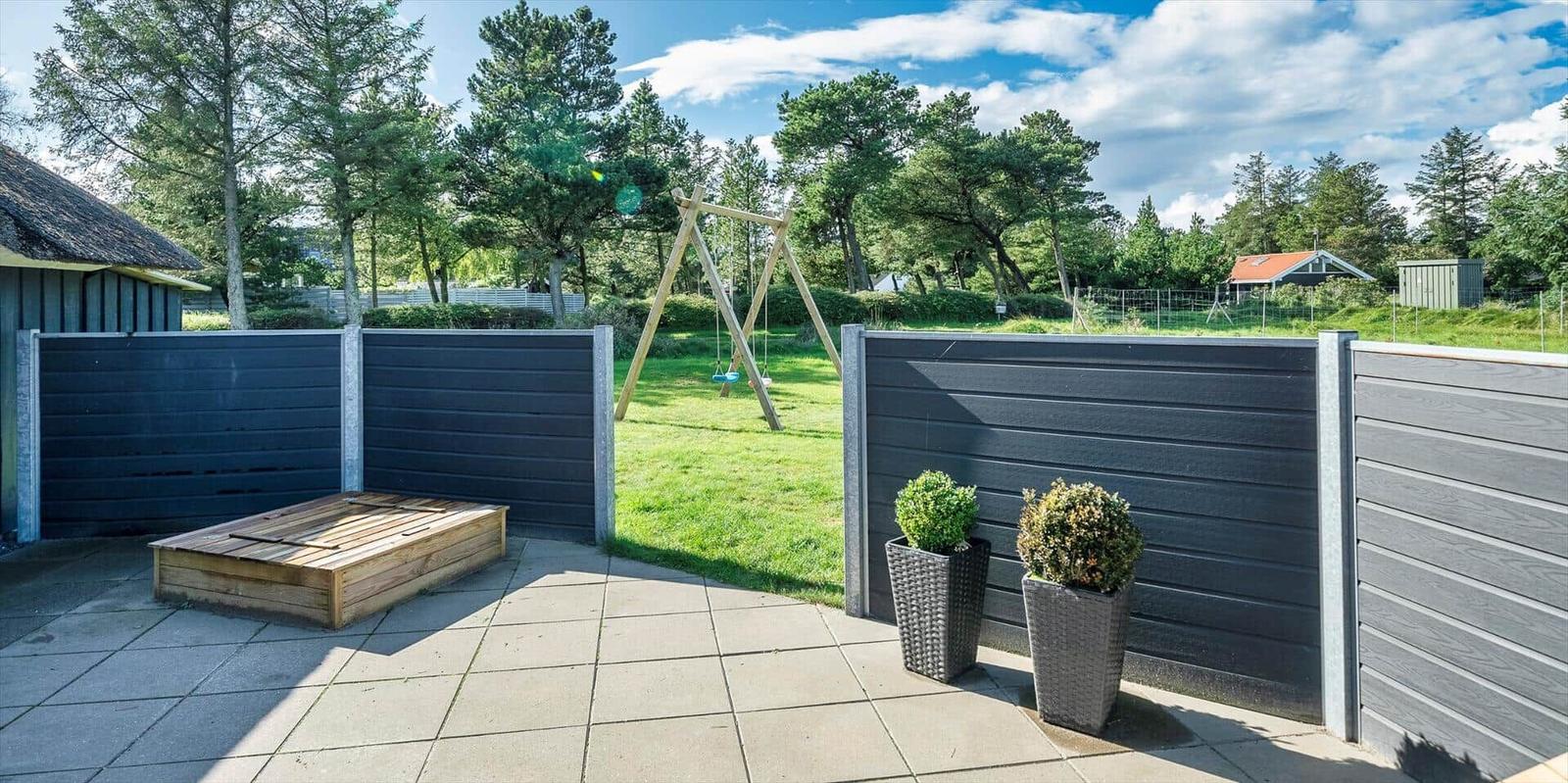 Terrasse mit Holzbank, Zaun und Spielplatz im Hintergrund.