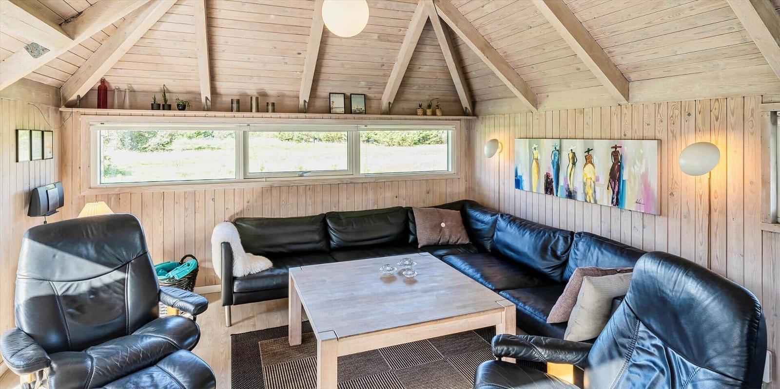 Wohnraum mit L-förmigem Sofa, zwei Sesseln und Holztisch unter Holzdecke.