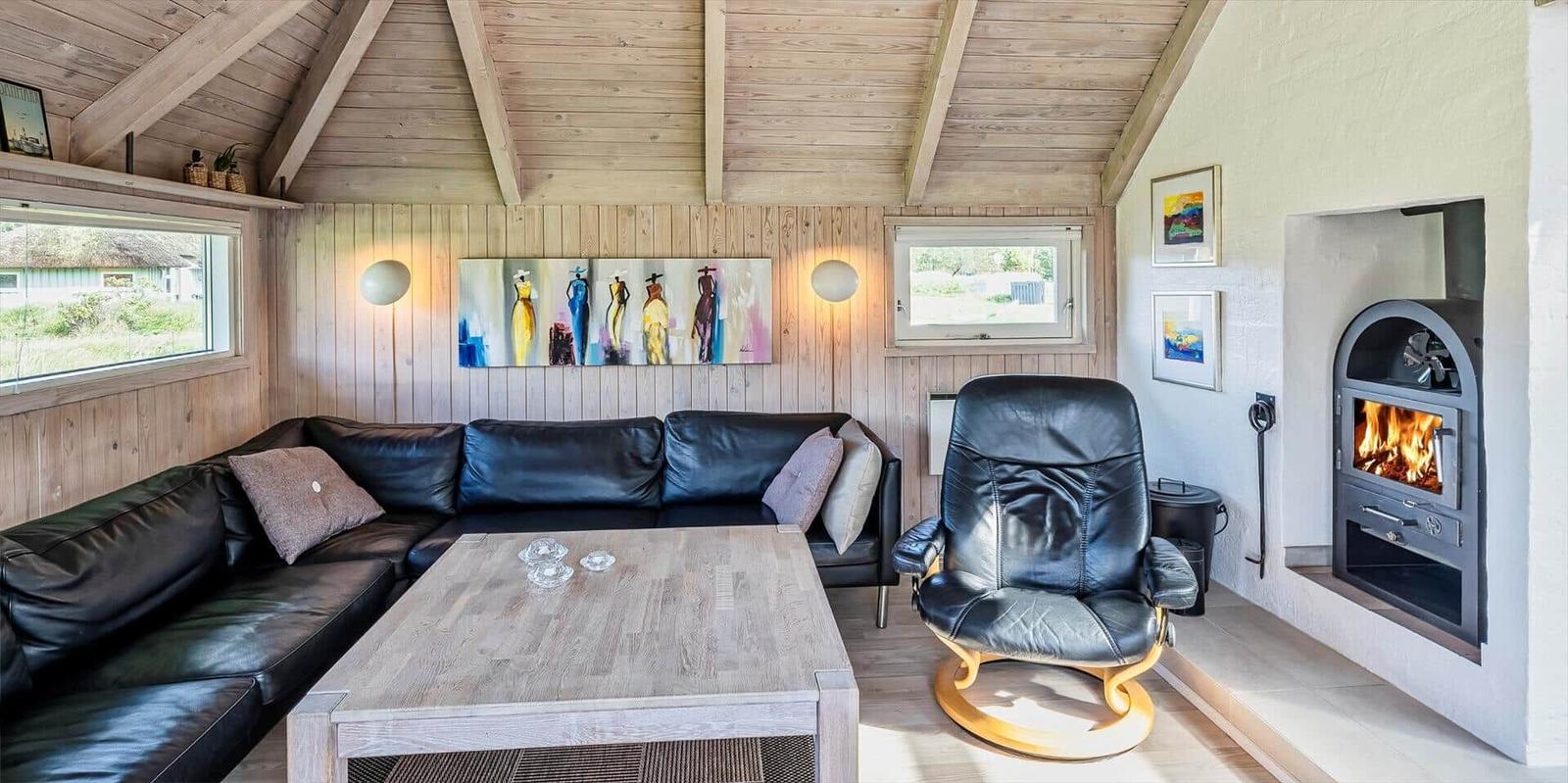 Wohnzimmer mit Ledersofa, Holztisch und Kaminofen. Holzwände und Dachschrägen.