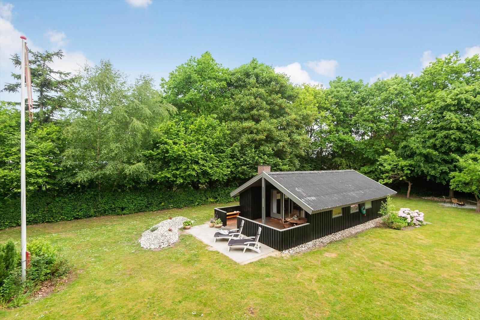 Schwarze Hütte mit Terrasse und Liegestühlen im grünen Garten.