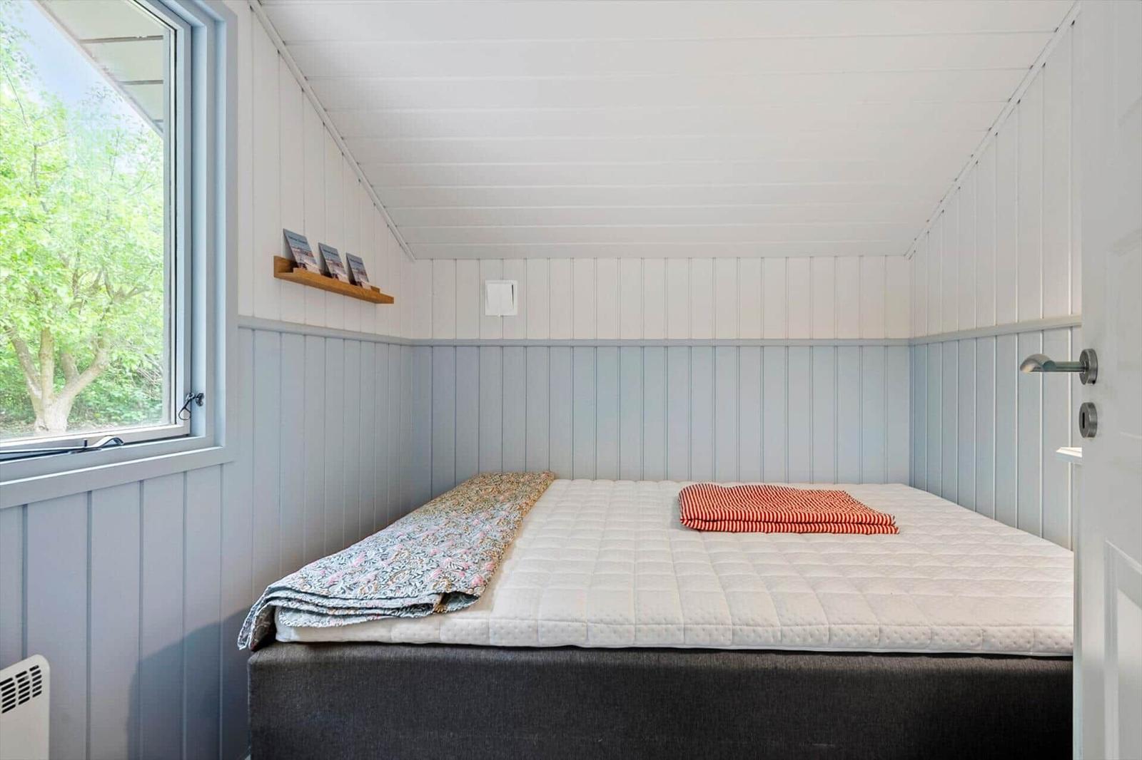 Schlafzimmer mit Bett, Fenster und Holzwandverkleidung.