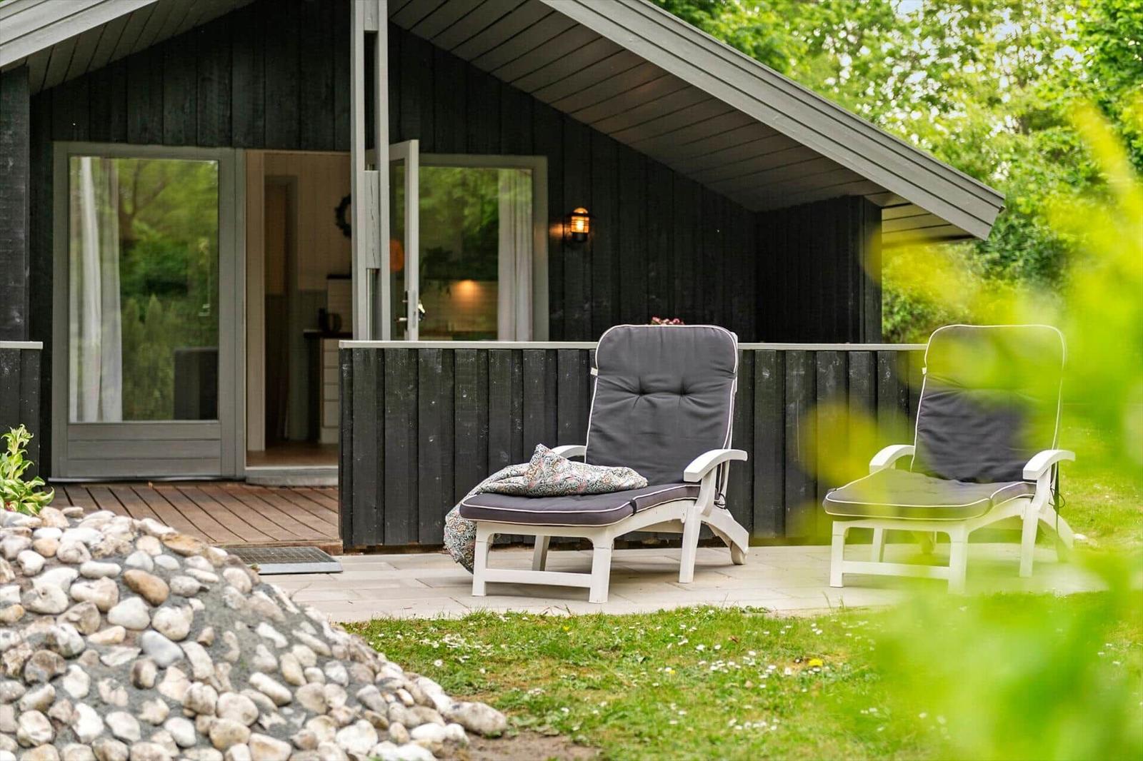 Terrasse mit zwei Liegestühlen vor einem Holzhaus mit Glasfront.