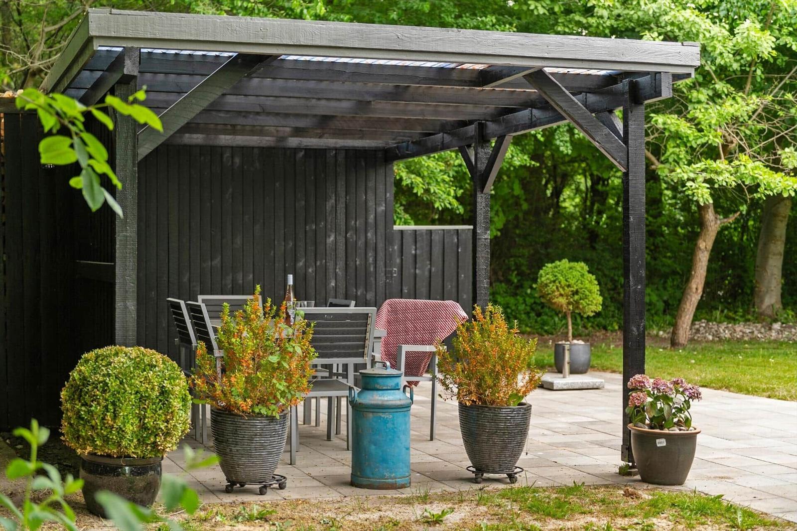 Garten mit Pavillon, Tisch, Stühlen und Pflanzen in großen Töpfen.