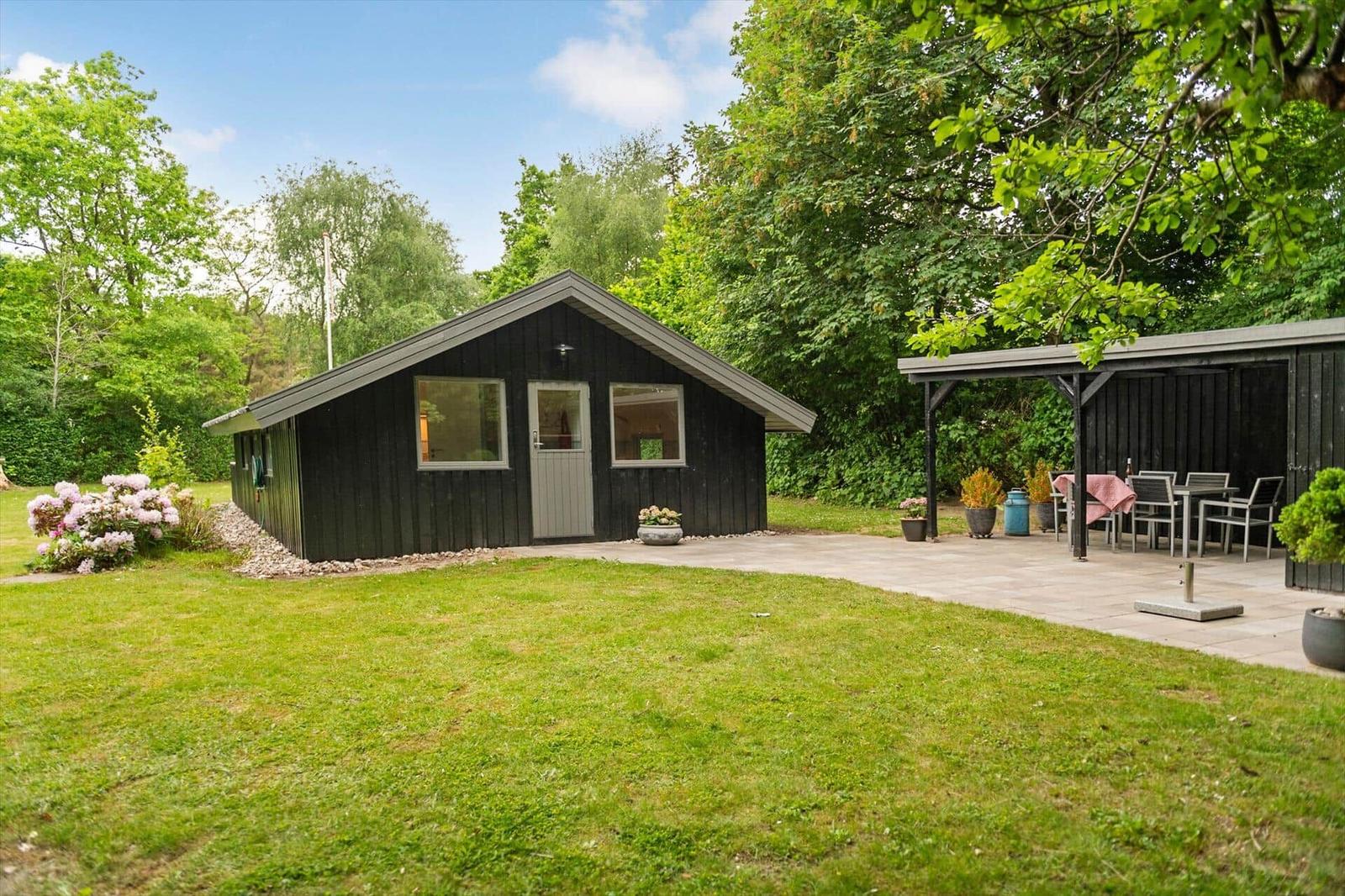 Schwarzes Holzhaus mit Terrasse und Garten. Außengelände mit Sitzgelegenheiten.