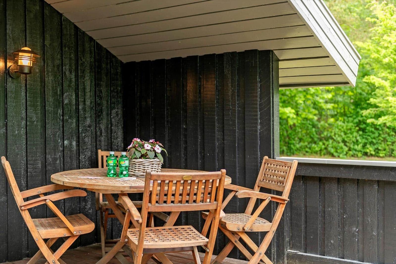 Terrasse mit Holztisch, vier Stühlen, Blumenkorb und zwei Wasserflaschen.