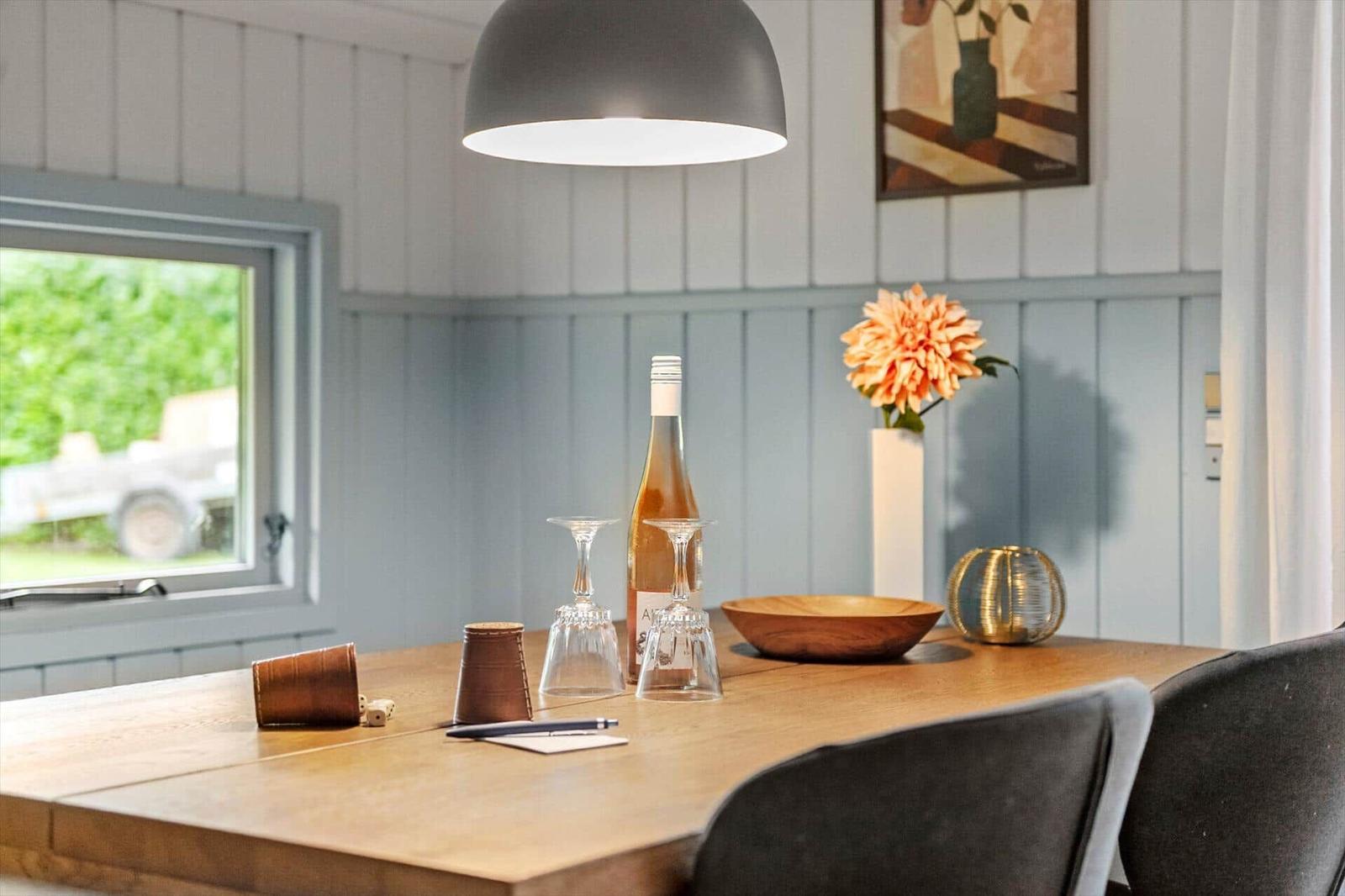 Holztisch mit Weinflasche, Gläsern und Blume. Hintergrund: Wand mit Holzverkleidung und Fenster.