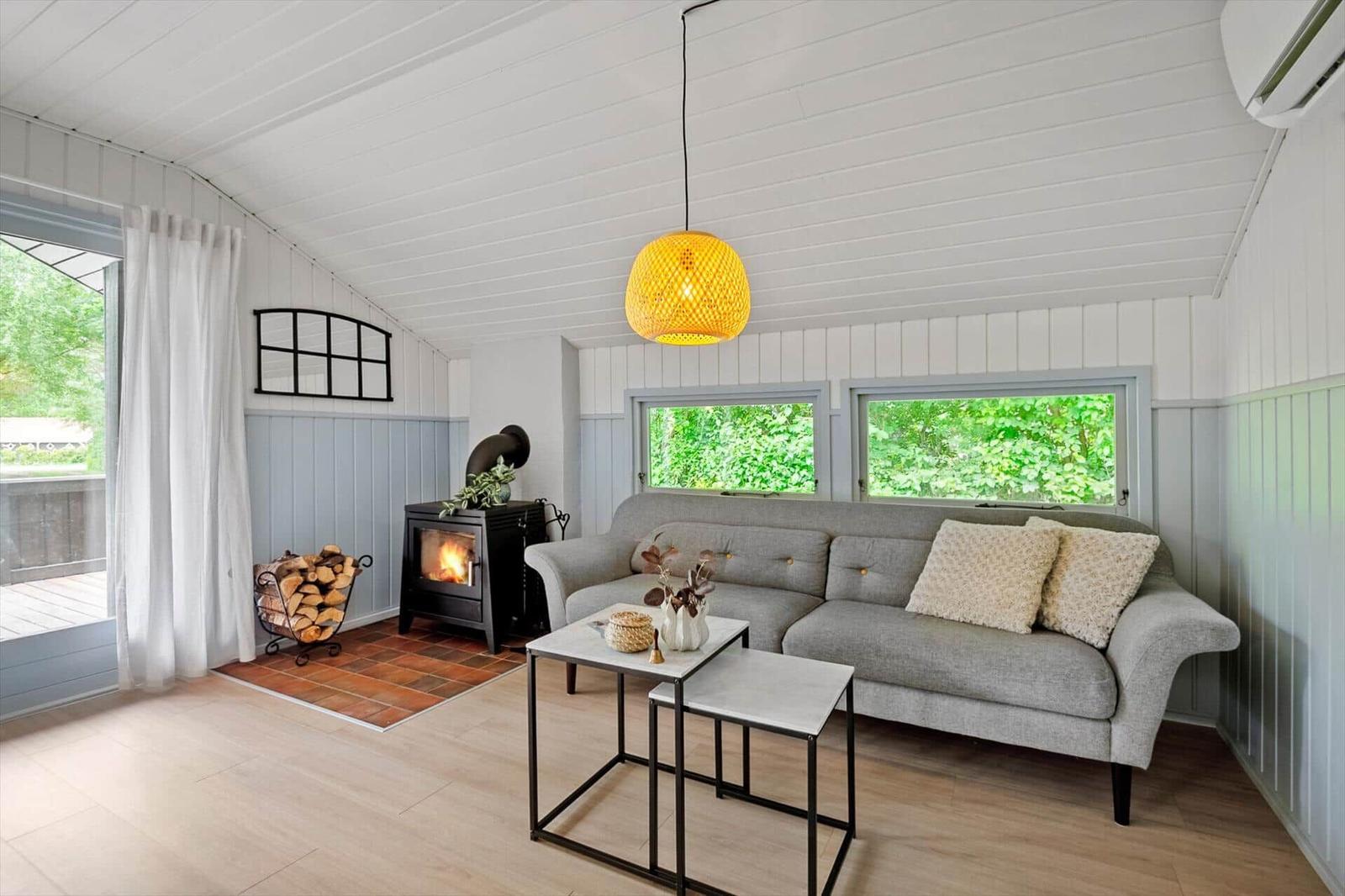 Wohnzimmer mit Sofa, Kamin und Fenstern zum Grün. Helle Wände und Holzboden.
