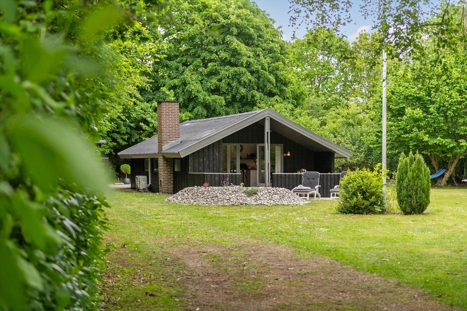 Moderne Holzhütte mit Terrasse und Garten. Umgeben von Bäumen und Gras.