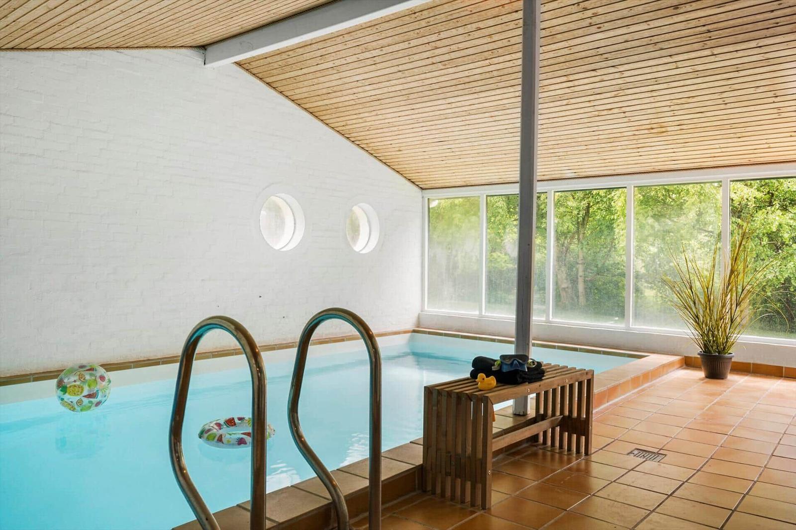 Innenpool mit Holzdecke, runden Fenstern und Blick auf Bäume.