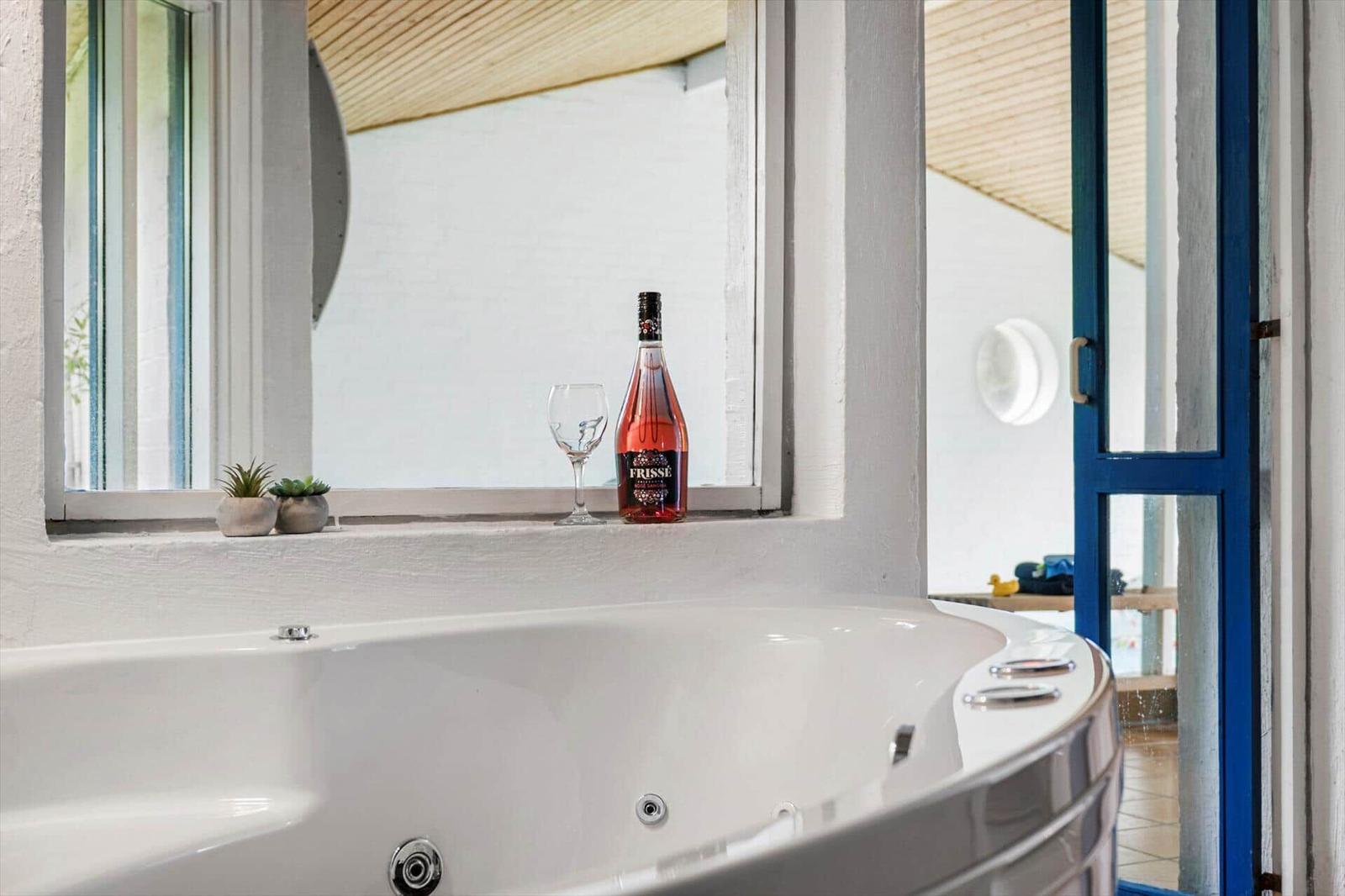 Whirlpool mit Flasche und Glas auf Fensterbank. Blick auf Außenbereich mit blauer Tür.