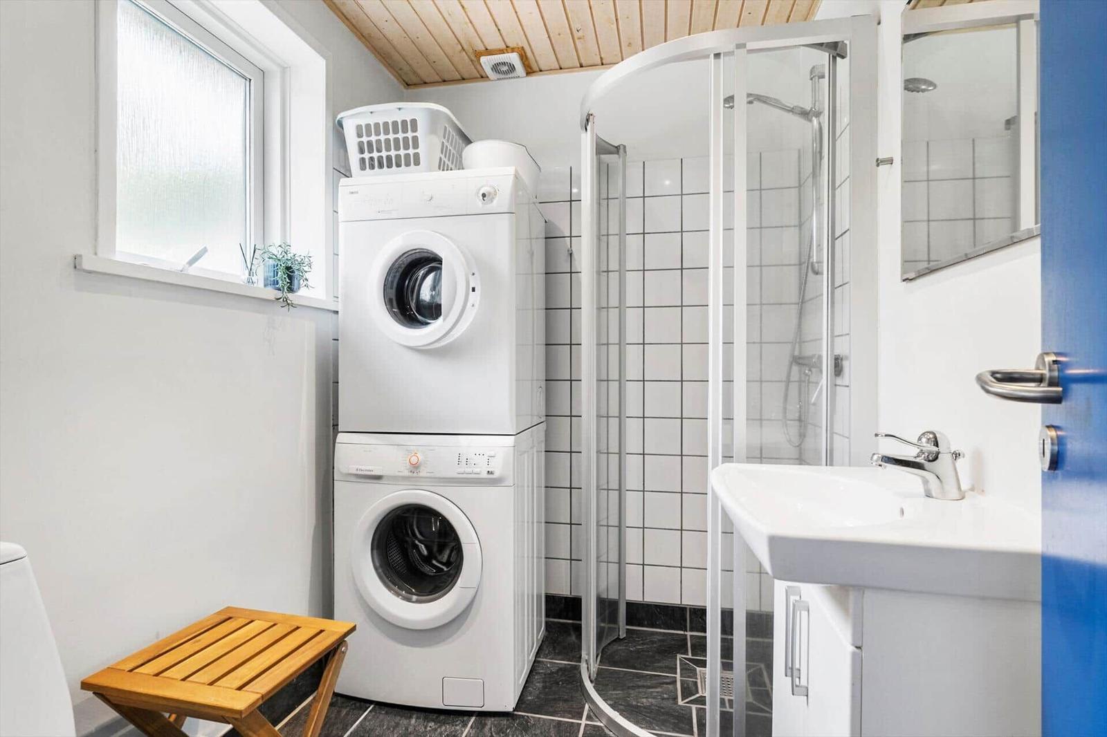 Badezimmer mit Dusche, Waschmaschine und Trockner. Holzdecke und Fenster.