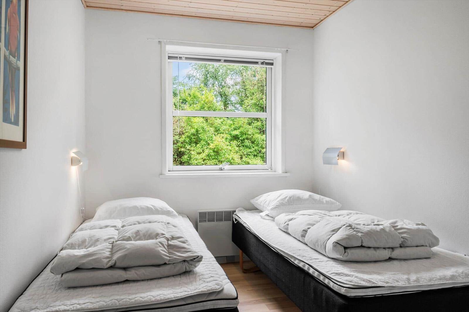Zwei Betten mit weißen Bettwäschen stehen unter einem Fenster mit Blick auf Bäume.