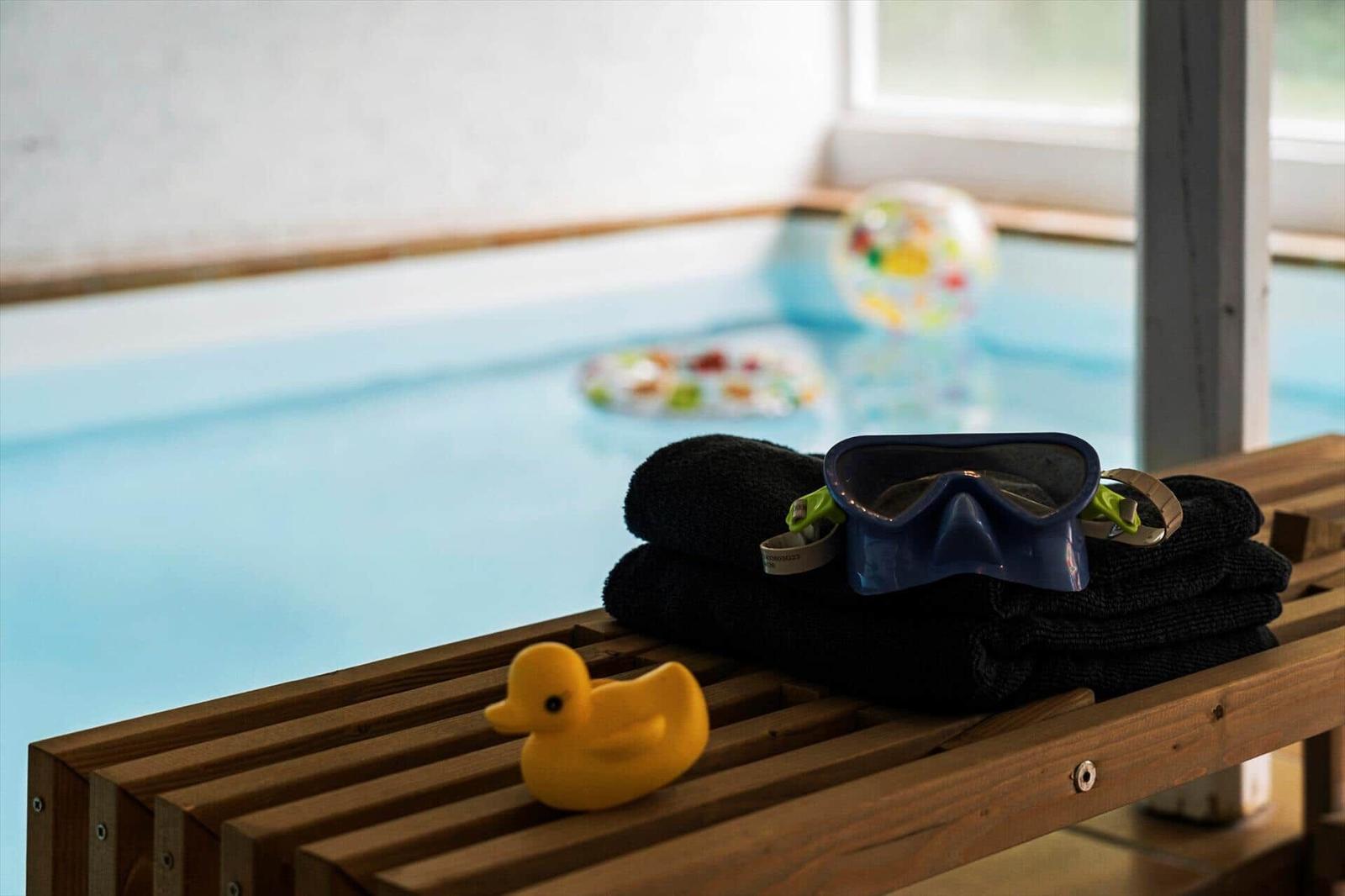 Schwimmbad mit Schwimmbrille, Handtuch und gelber Ente auf Holzbank.