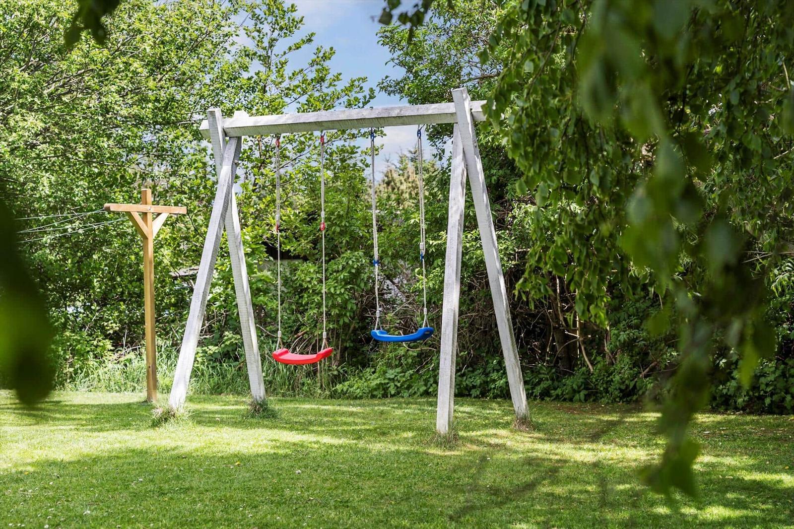 Ein weißer Schaukelstand mit roter und blauer Schaukel auf einer grünen Wiese.