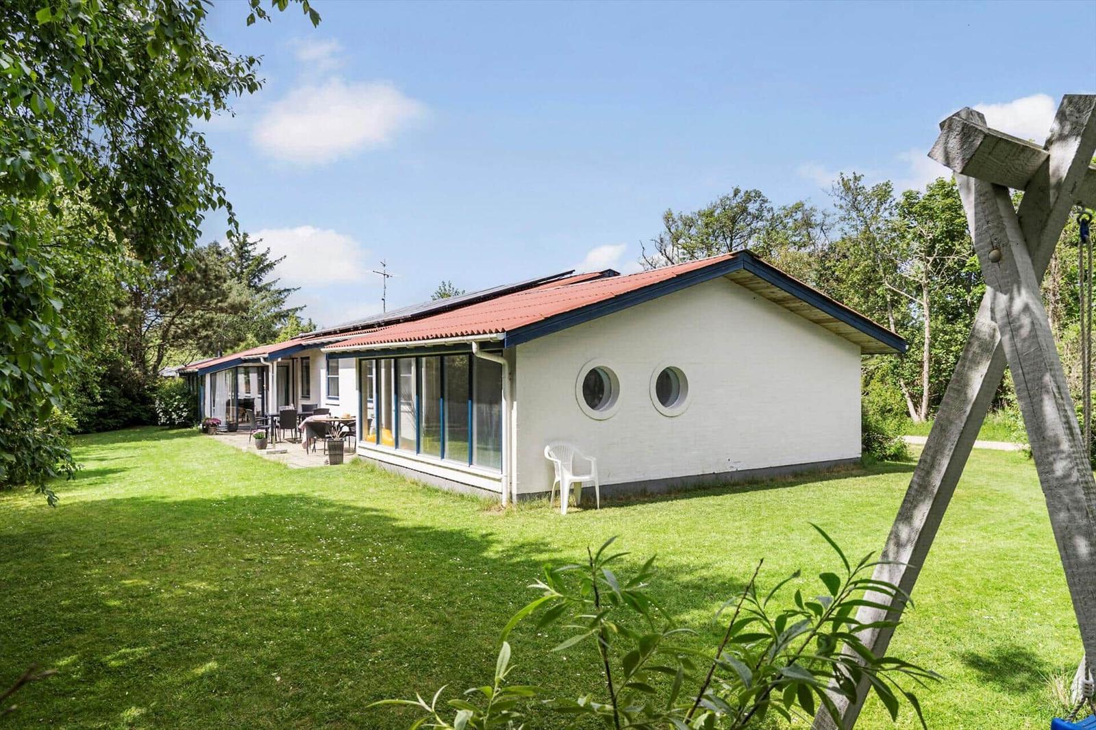 Ein weißes Haus mit runden Fenstern und rotem Dach auf einer grünen Wiese.