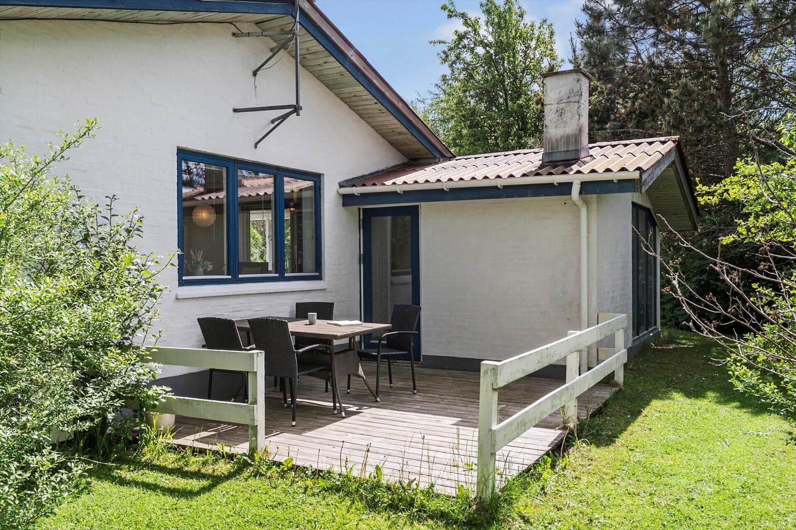 Wohnhaus mit Terrasse, Tisch und Stühlen, umgeben von Grün und Bäumen.
