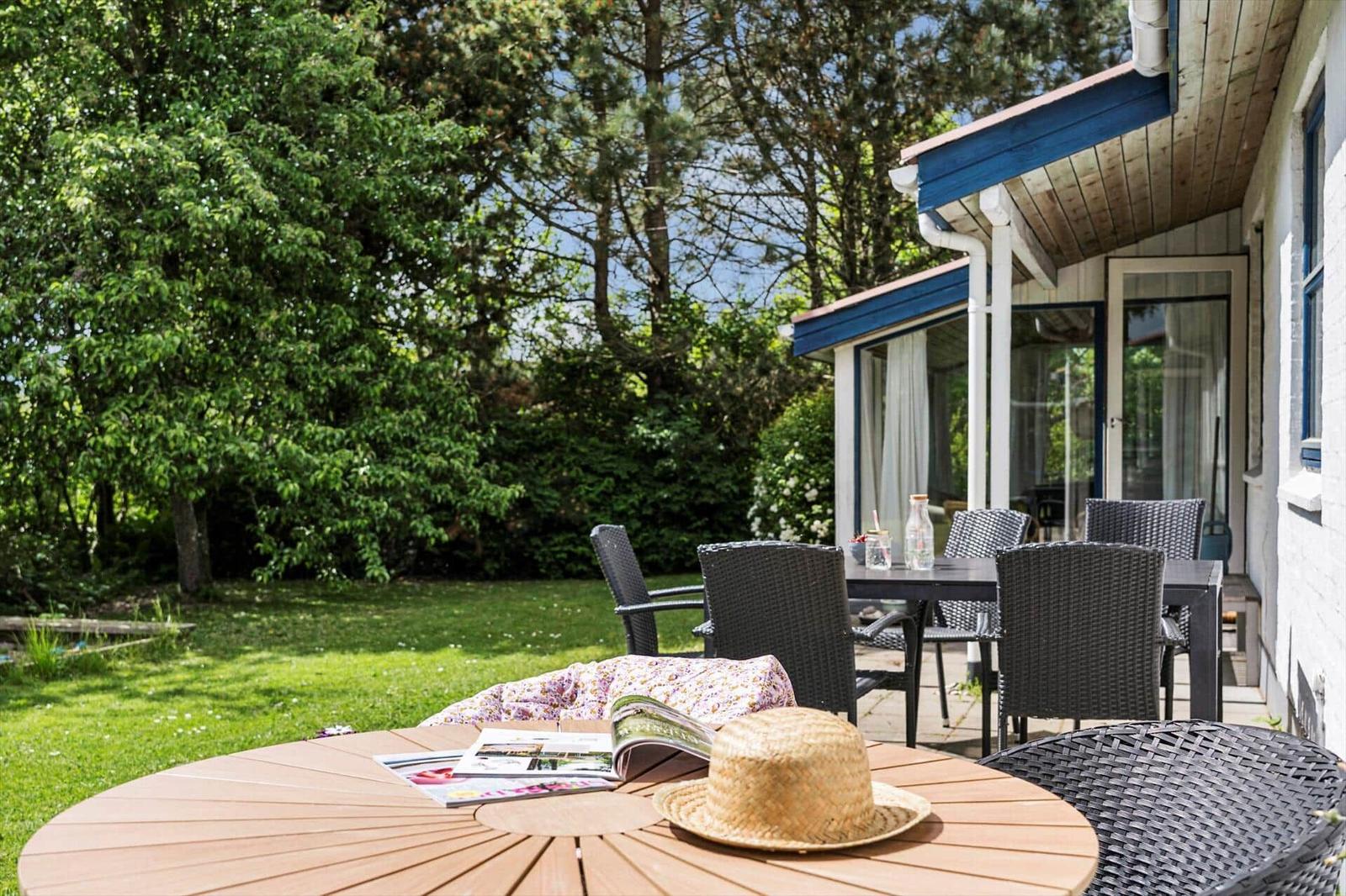 Terrasse mit Sitzgruppe und Garten. Holztisch mit Strohhut und Zeitschrift.