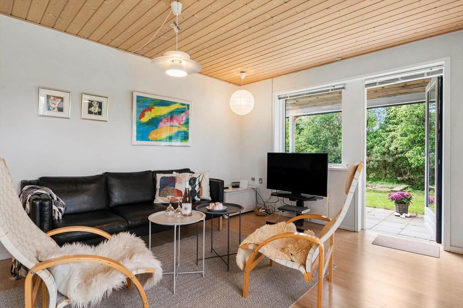 Wohnzimmer mit Sofa, zwei Stühlen, Fernseher und Blick auf Garten.