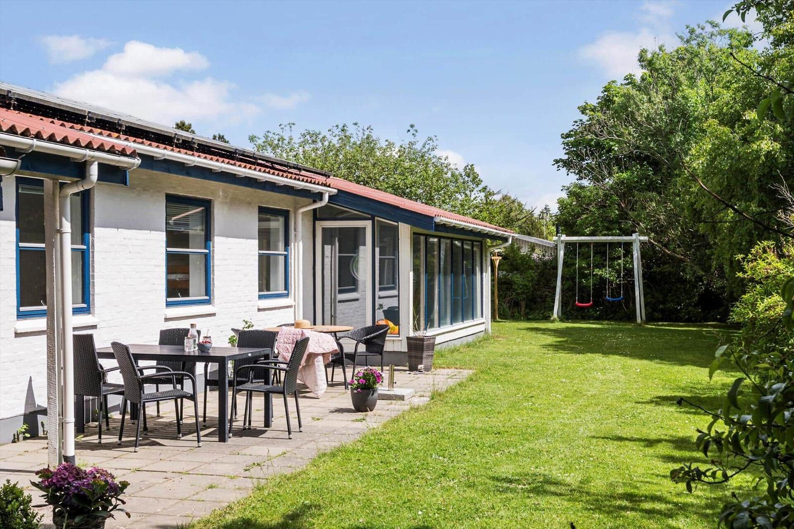 Wohnhaus mit Terrasse, Garten und Schaukel. Tisch und Stühle stehen draußen.