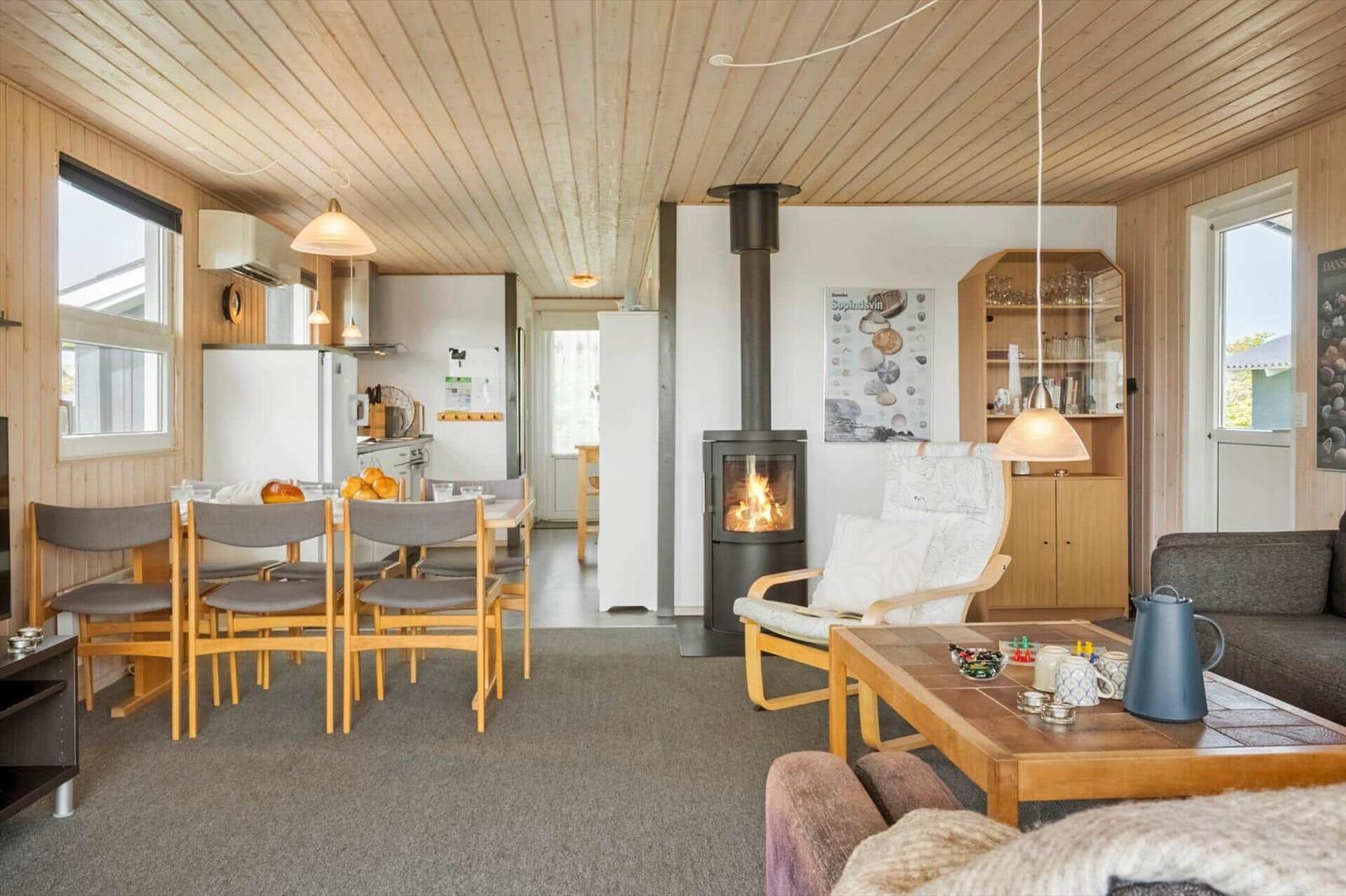 Wohnzimmer mit Kamin, Esstisch und Küchenbereich. Holzdecke und Möbel.