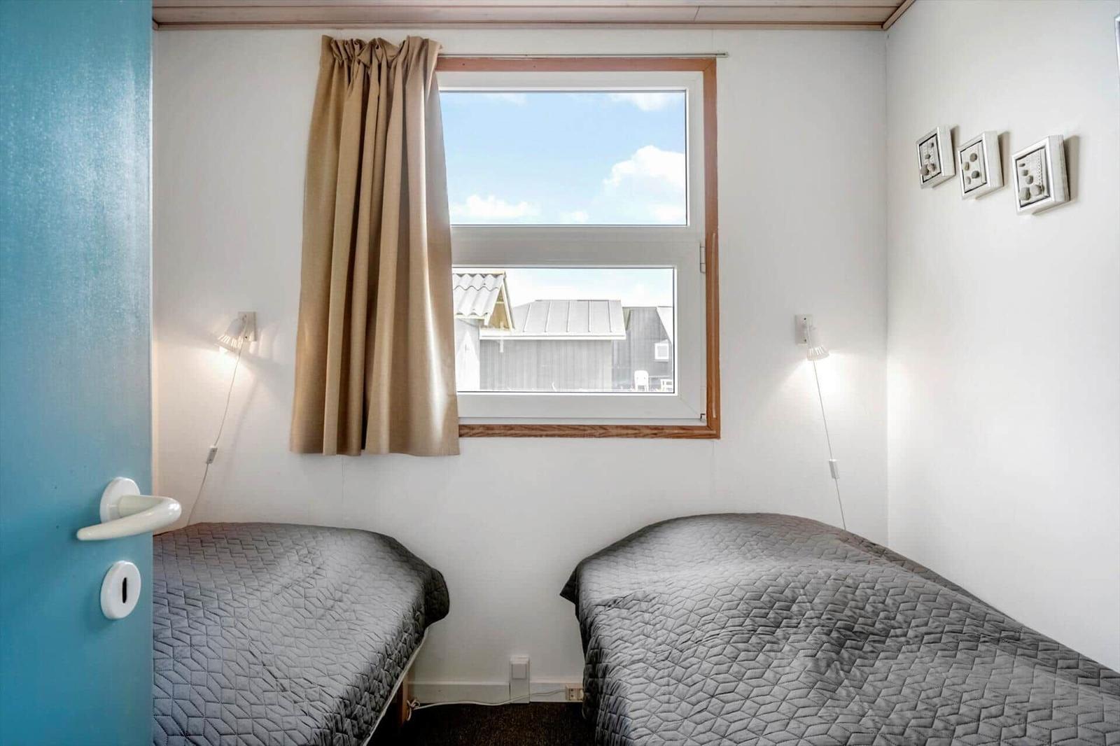 Zwei Betten mit grauer Bettwäsche stehen unter einem Fenster mit braunen Vorhängen.