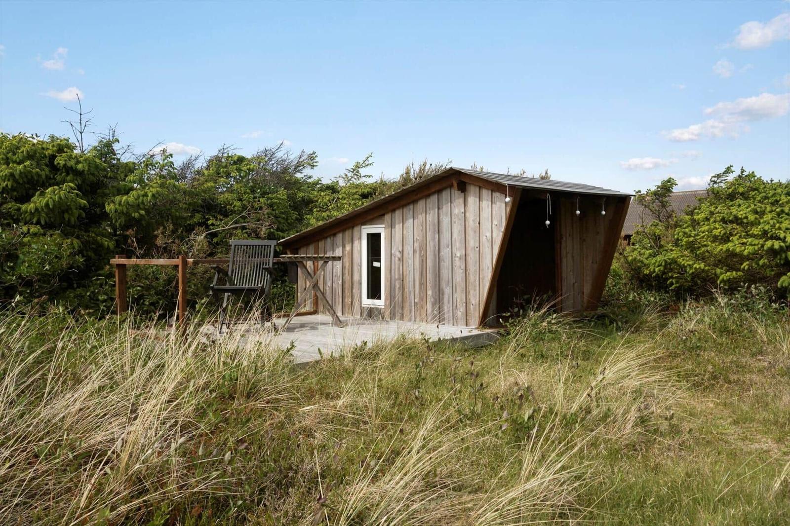 Holzhütte mit Terrasse und Stuhl in Grasland unter blauem Himmel