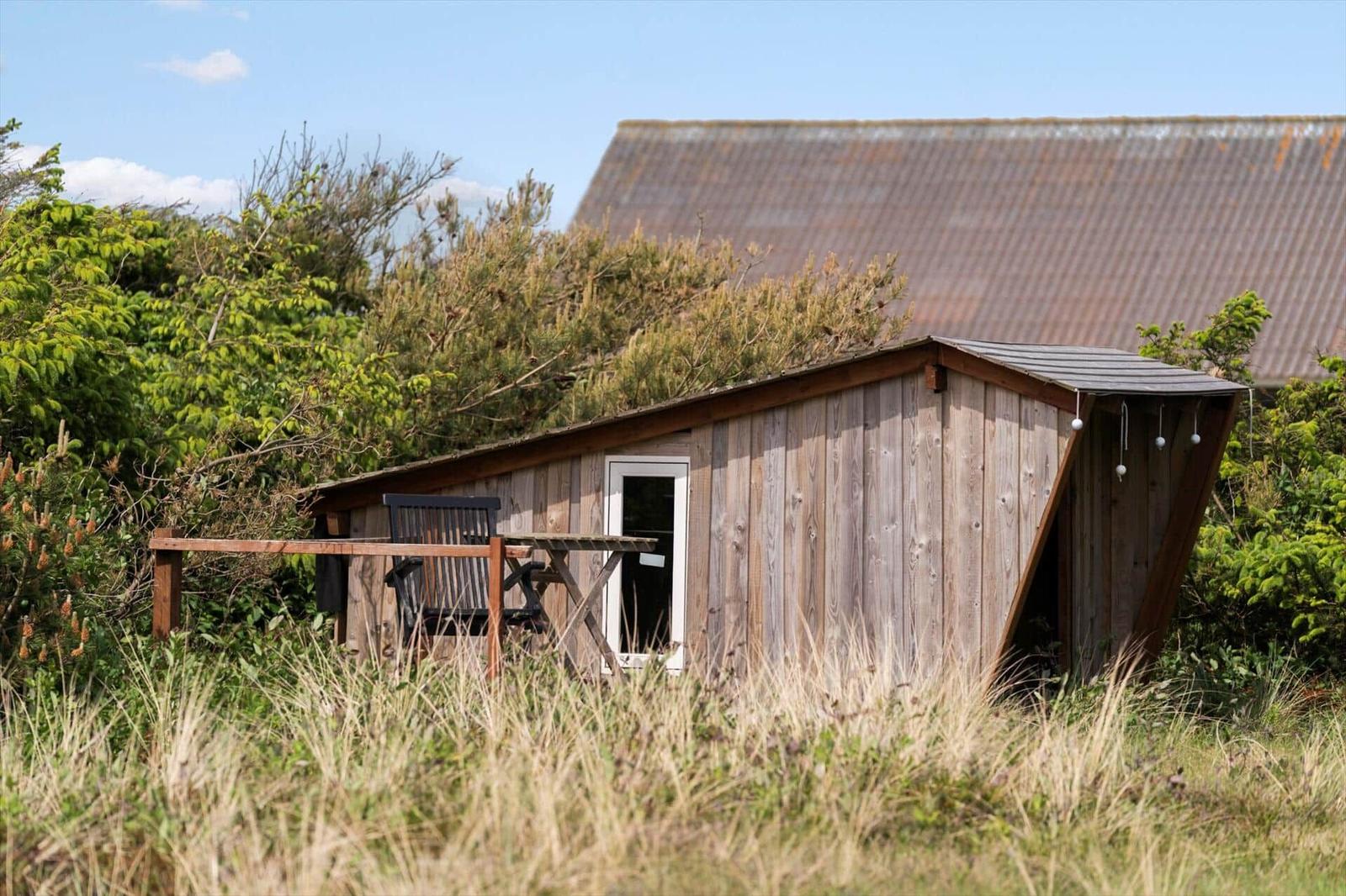 Holzhaus mit Terrasse, Tisch und Stuhl im Gras. Hintergrund: rustikales Gebäude.