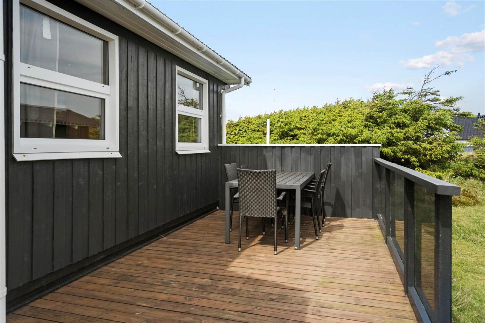 Terrasse mit Tisch und Stühlen neben einem Haus mit dunkler Holzfassade.