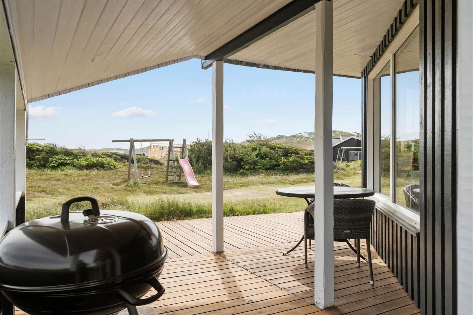 Terrasse mit Grill, Tisch und Stühlen. Im Hintergrund Spielplatz und Grünland.
