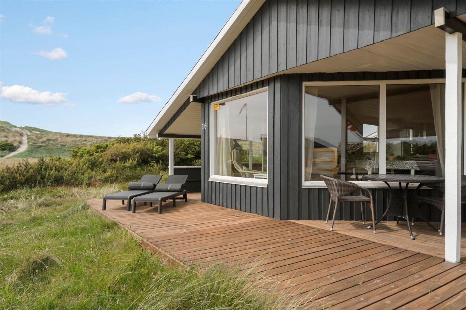 Terrasse mit Liegestühlen und Tisch. Haus mit großen Fenstern und Holzveranda.