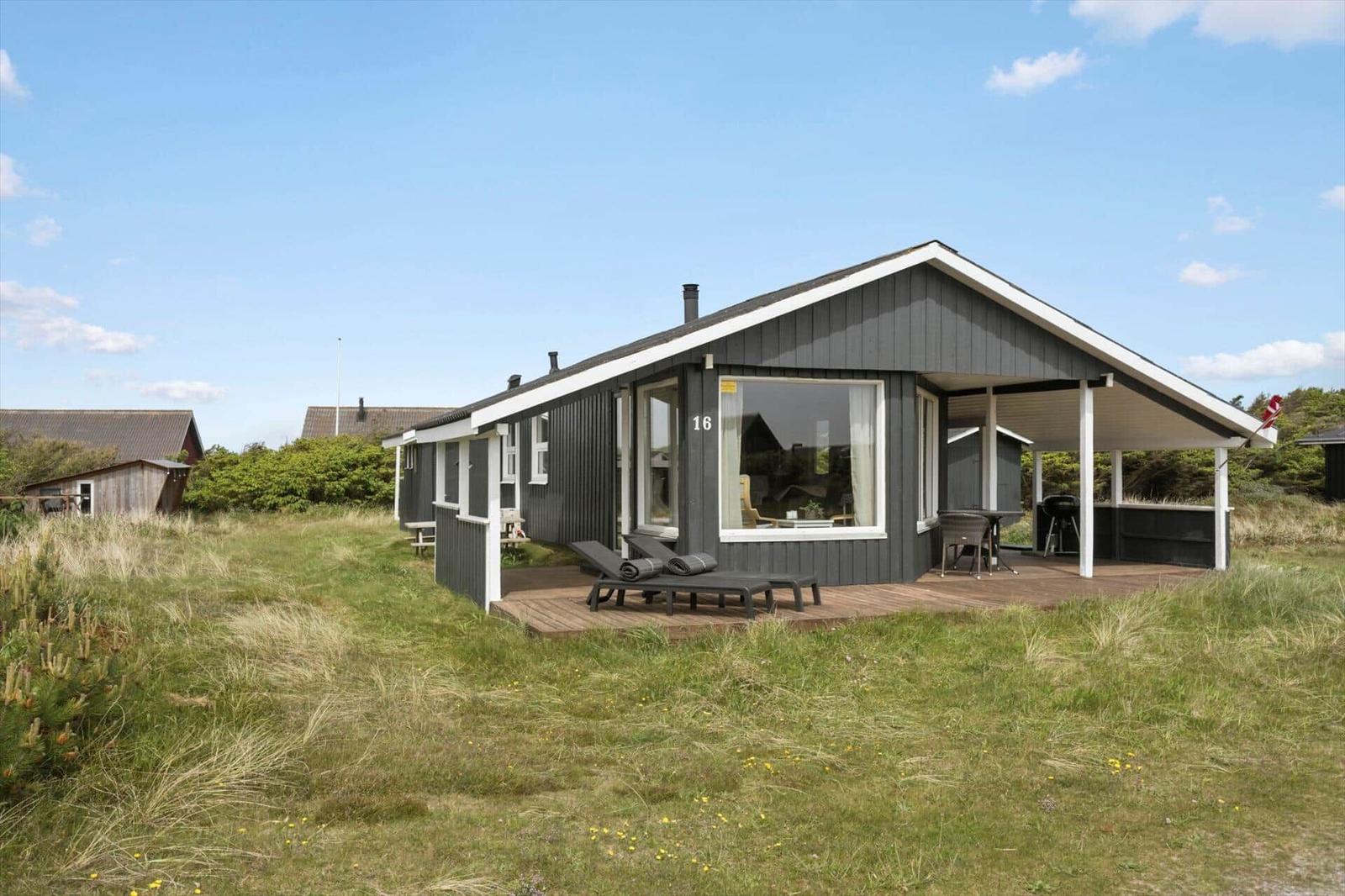 Ein modernes Ferienhaus mit Terrasse, Liegen und Grillplatz in einer grünen Umgebung.