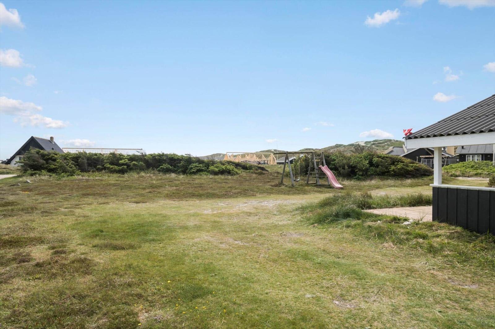 Grüner Garten mit Spielplatz und Blick auf Dünen.