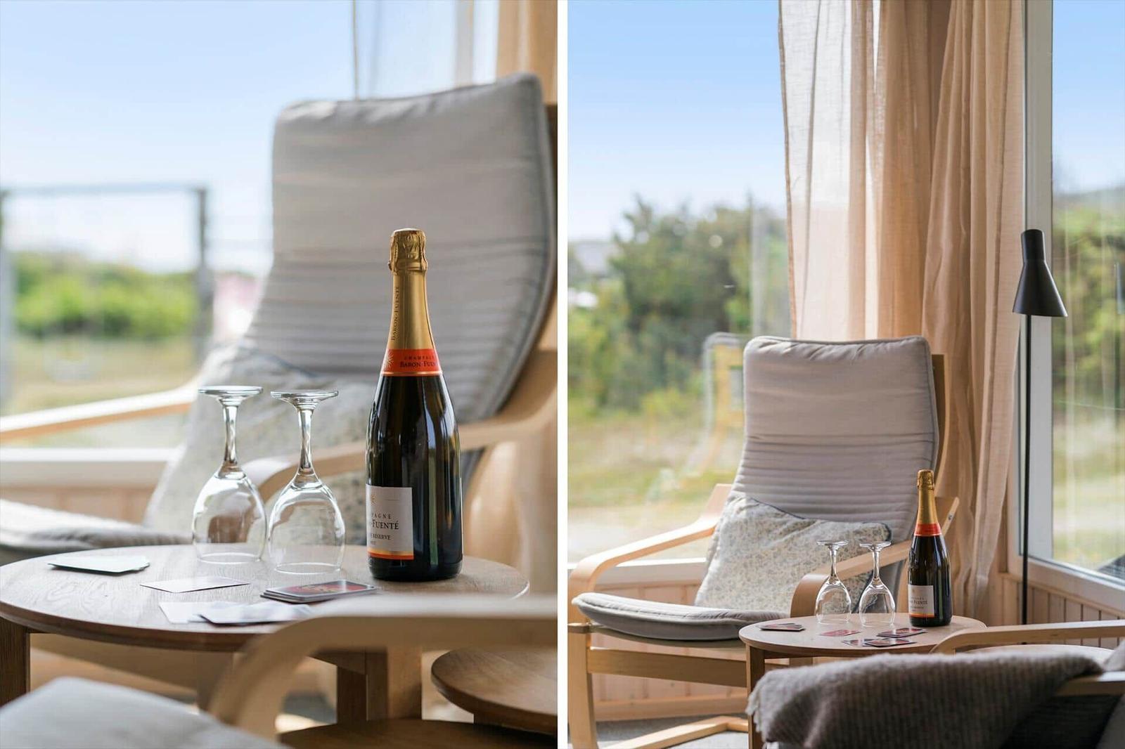 Eine Flasche Sekt mit zwei Gläsern auf einem Tisch vor einem Fenster mit Blick nach draußen.