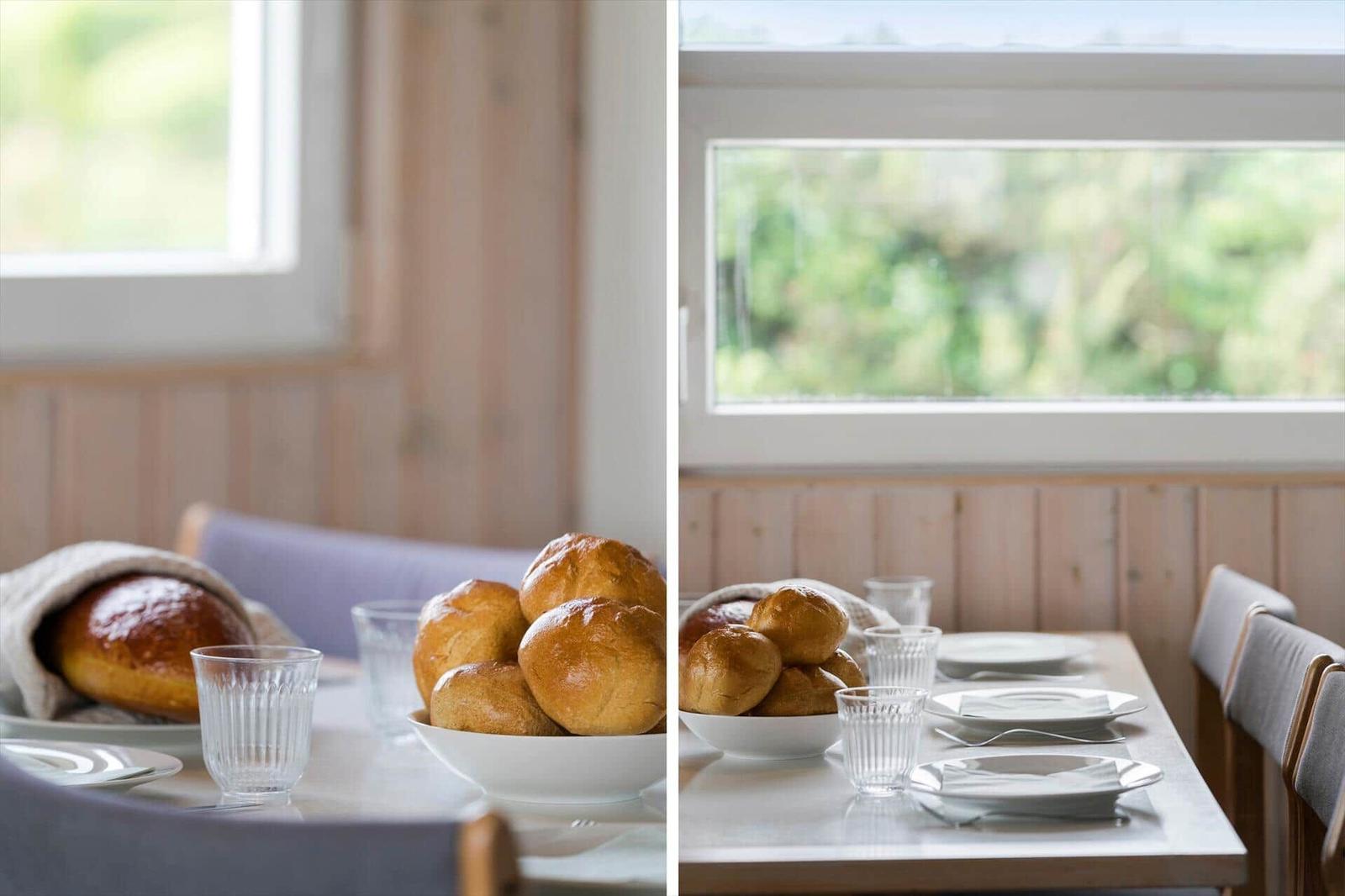 Tisch mit Brot, Gläsern und Tassen vor Fenster mit Blick auf Grün.