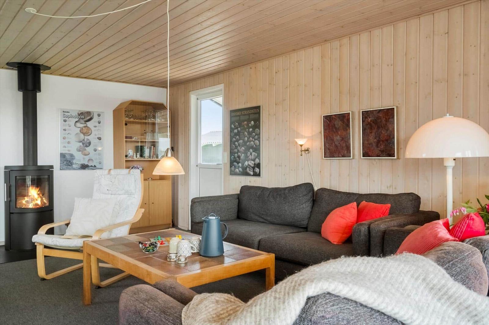 Wohnzimmer mit Sofa, Kamin und Holzwand. Tisch mit Teekanne und Kissen.