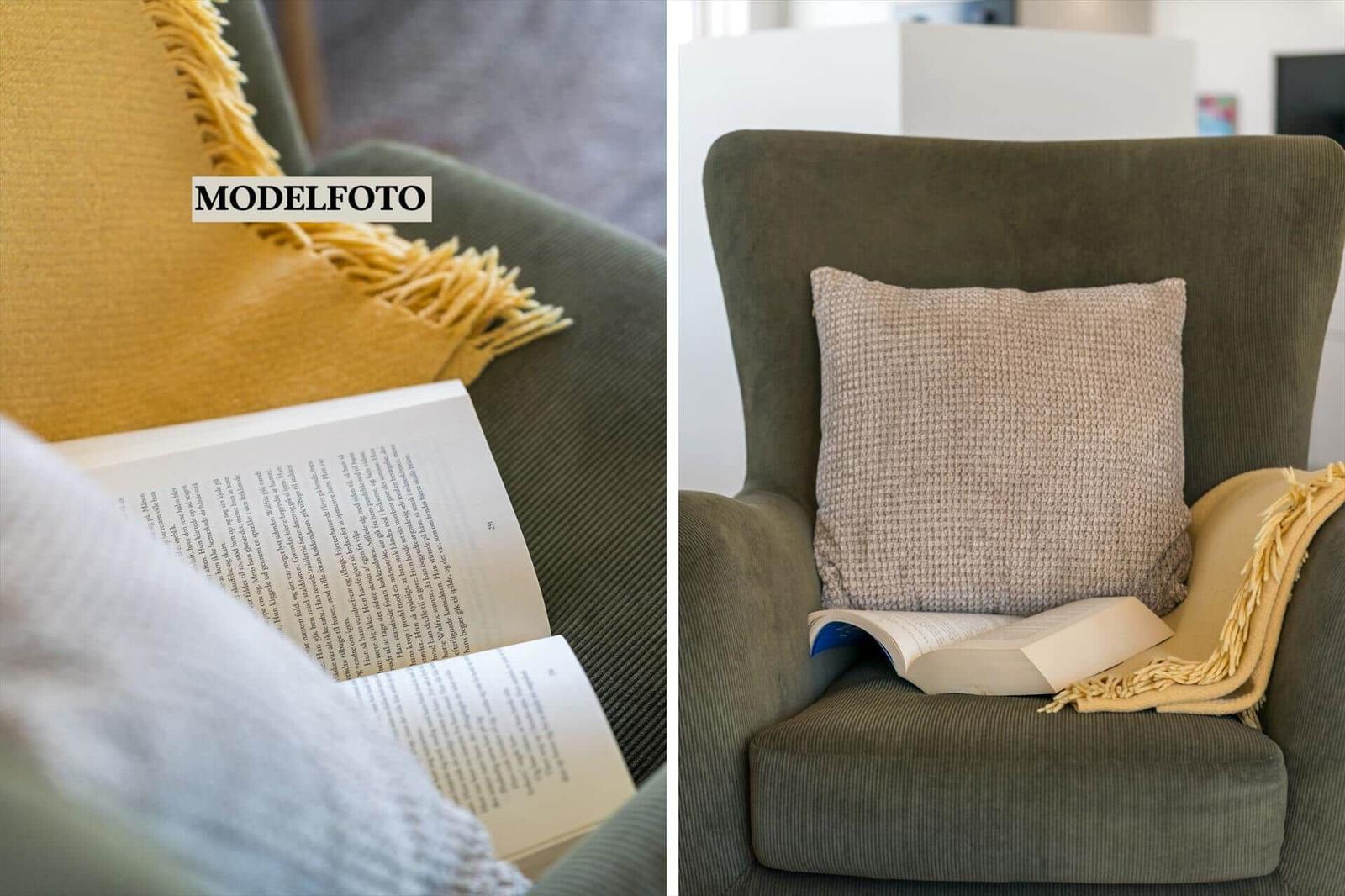 Ein grüner Sessel mit Kissen und Decke. Ein Buch liegt darauf.