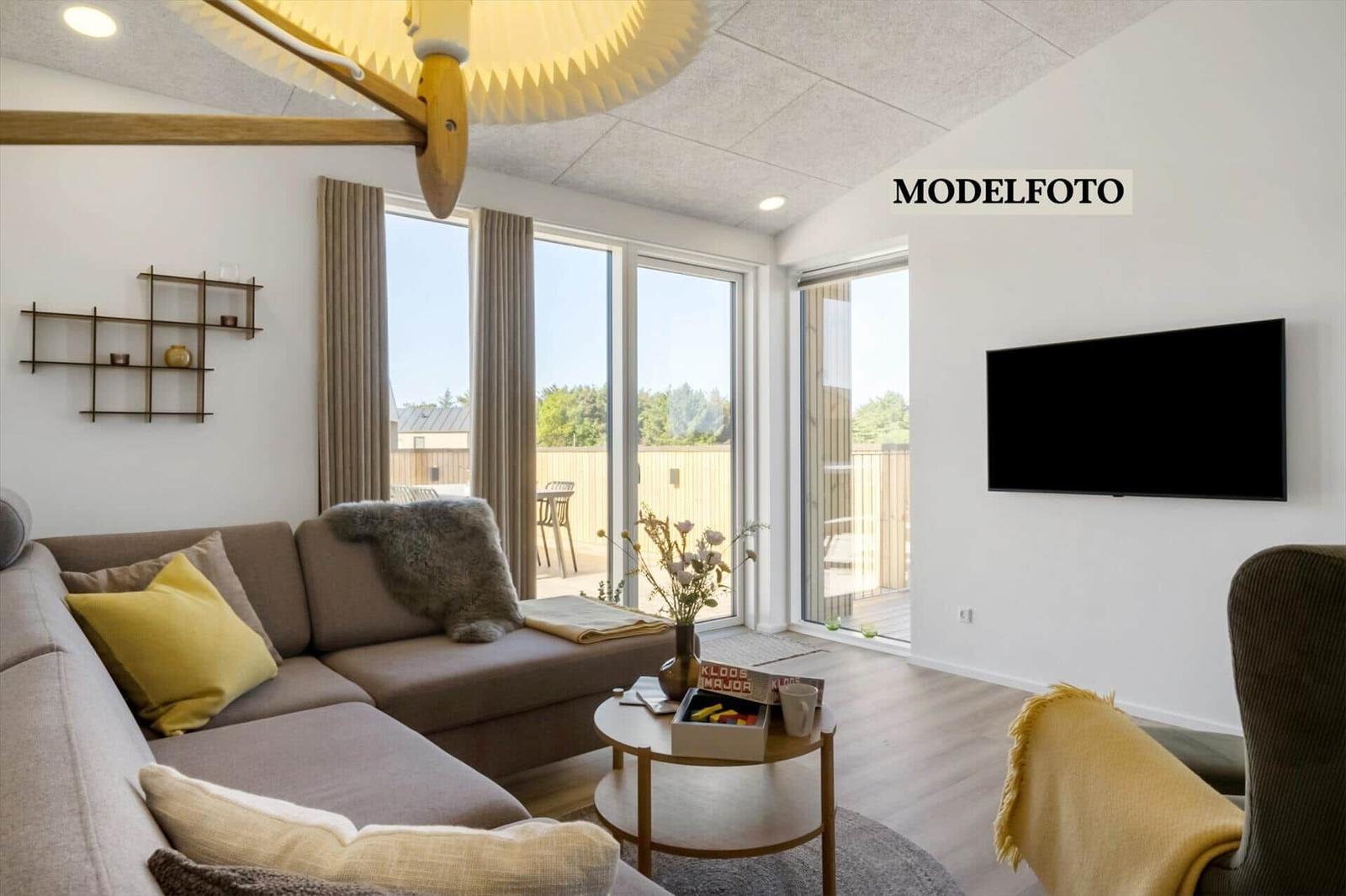 Wohnzimmer mit Sofa, Couchtisch und TV. Große Fenster mit Blick auf Balkon.
