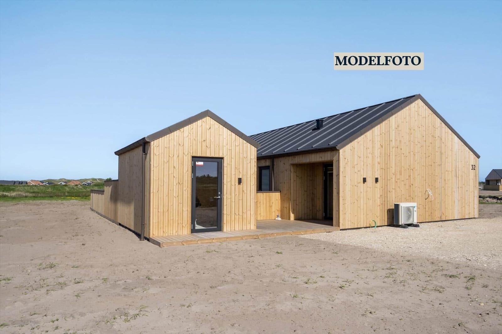 Holzhaus mit dunklem Dach und Eingangstür. Außenbereich mit Sand und Gras.